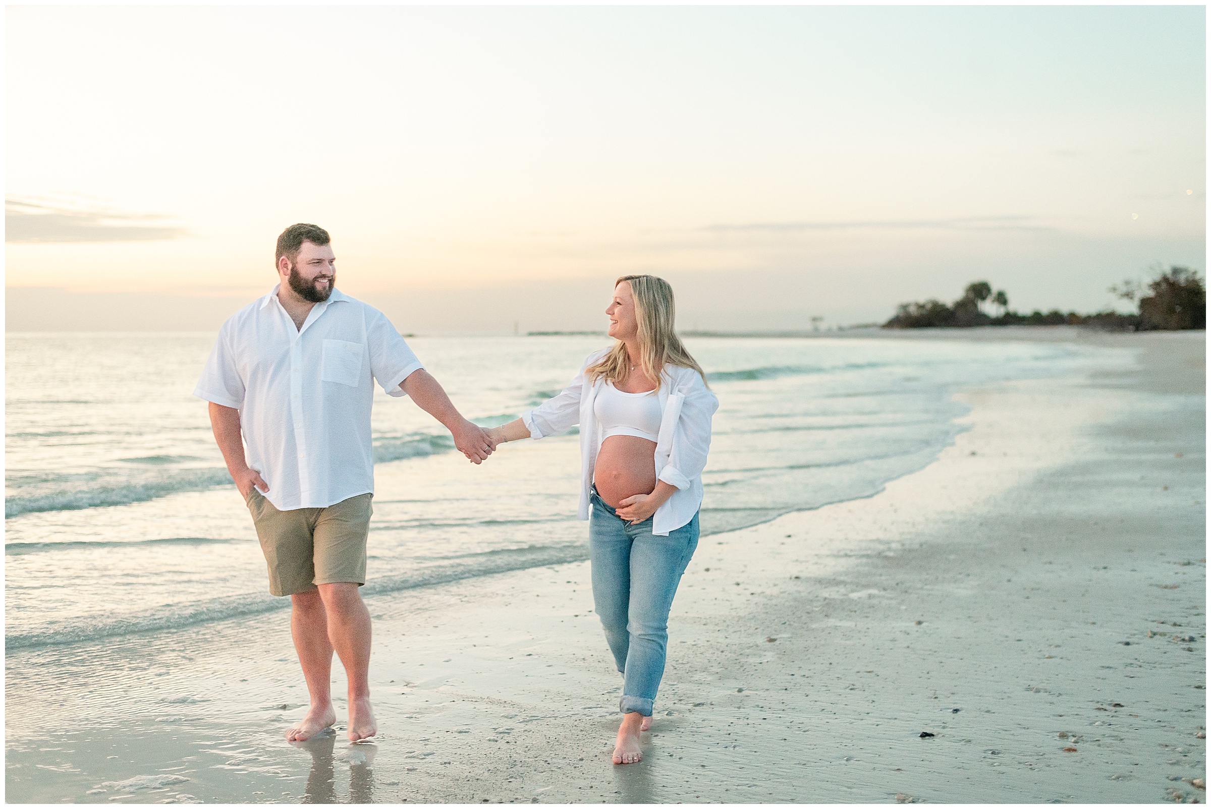 A couple walking together on the beach for their maternity photos at Honeymoon Island State Park in Florida. 