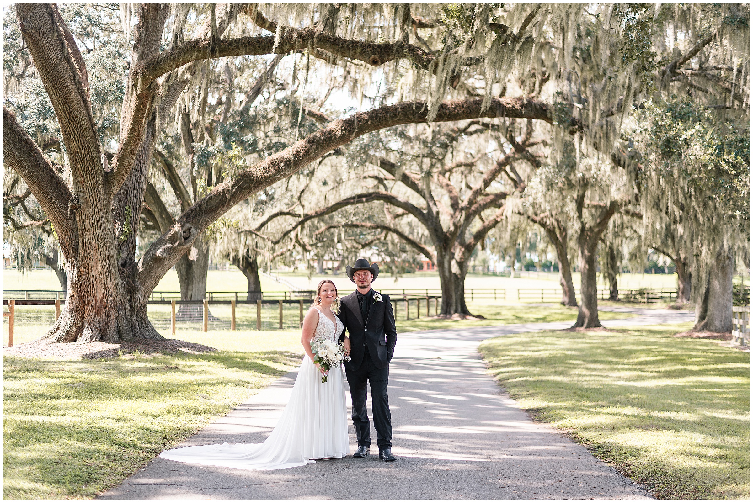 A bride and groom standing beside each other and smiling at the camera underneath huge oak trees at their Ocala Wedding at Protea Weddings and Events. 