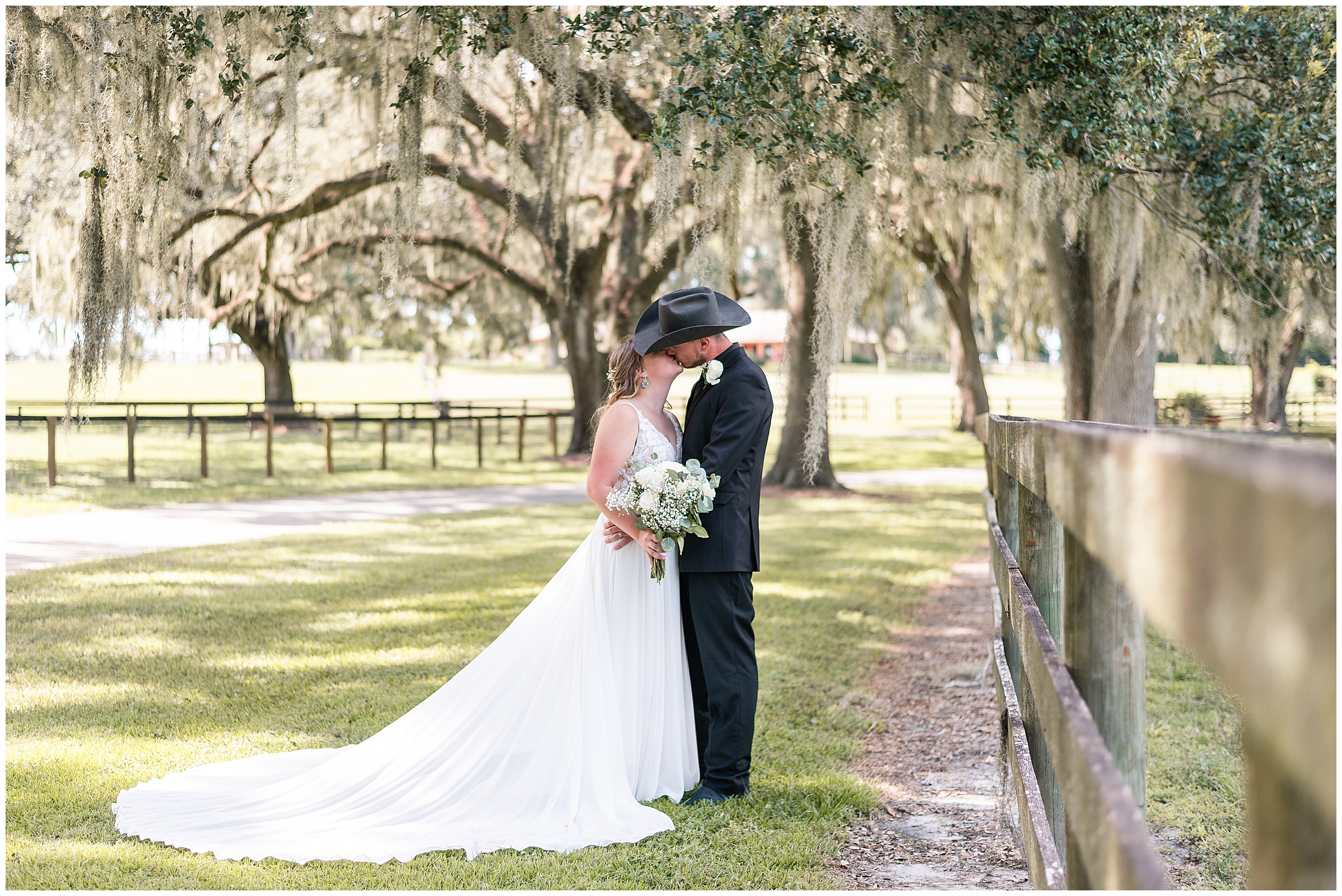 A bride and groom kissing underneath oak trees and along a wooden fence line at their Ocala Wedding at Protea Weddings and Events. 