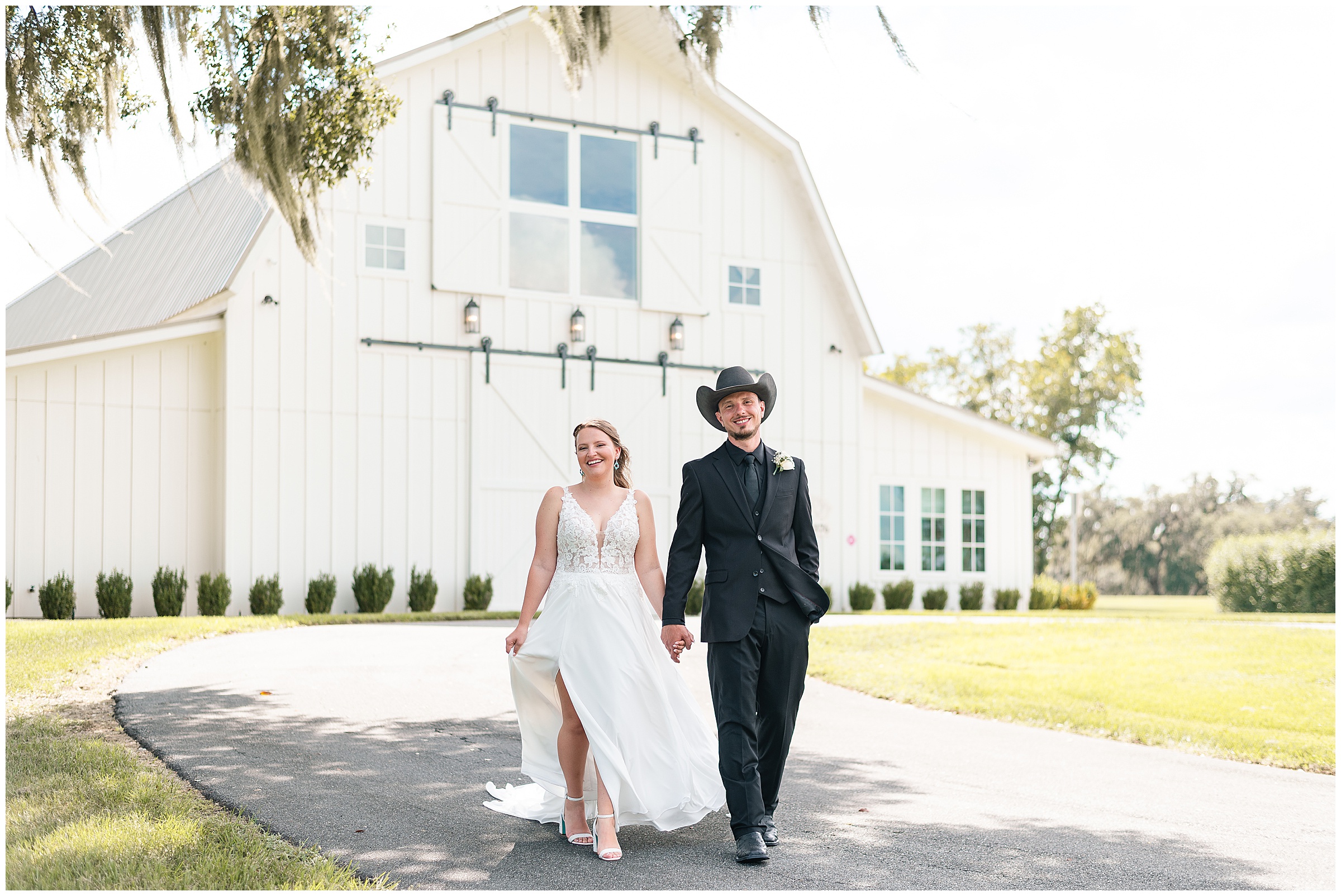 A bride and groom walking and smiling in front of the white barn at their Ocala Wedding at Protea Weddings and Events. 