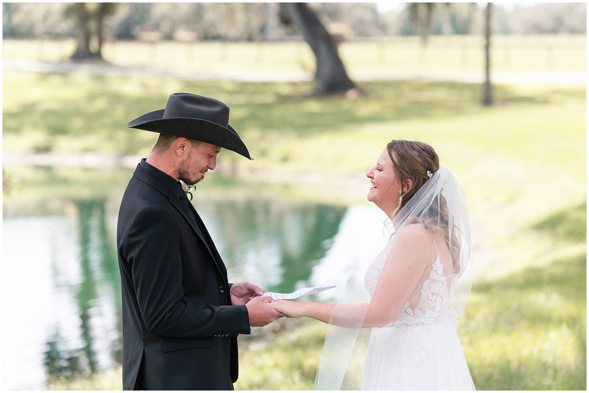 A bride and groom laughing together as the groom reads his vows to her. 
